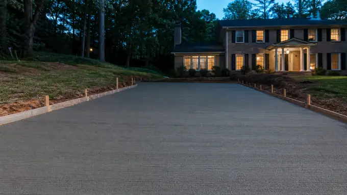 A broom drags across a driveway creating a slip-resistant texture. at a tan-brick colonial in Alpharetta, GA, at blue hour.