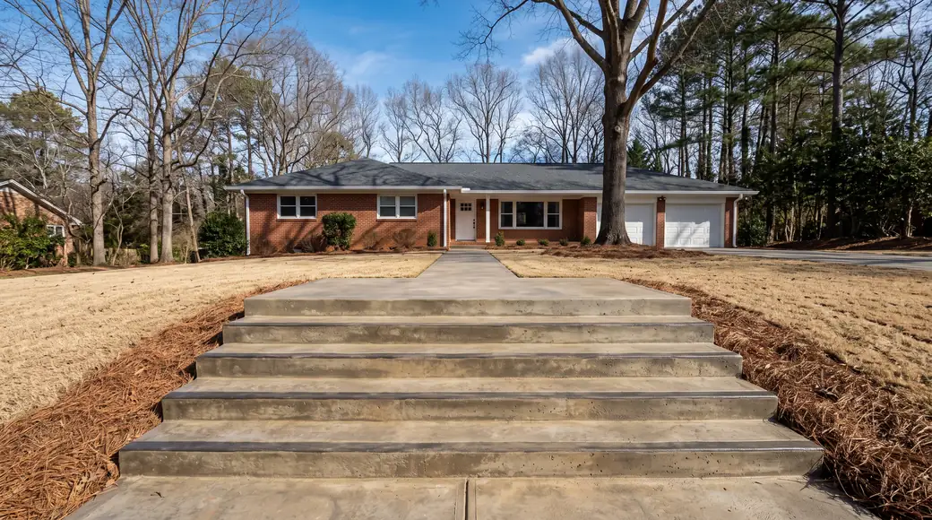 Poured concrete front steps rising to a landing at the front door at a red-brick ranch home in Alpharetta, GA, in clear late-morning sun.