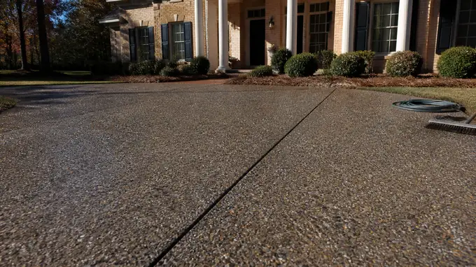 Newly washed exposed aggregate driveway with the stone just revealed at a tan-brick colonial in Alpharetta, GA, in clear late-morning sun.