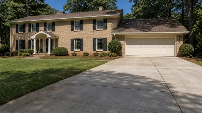 Settled garage approach slab the estimate would price to replace at a tan-brick colonial in Alpharetta, GA, in clear late-morning sun.