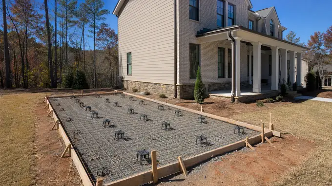 Patio forms squared up with reinforcing mesh on chairs at a brick-and-siding two-story home in Alpharetta, GA, in clear late-morning sun.