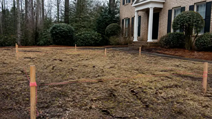 A contractor checks slope and drainage before work begins. at a tan-brick colonial in Alpharetta, GA, after a rain shower.