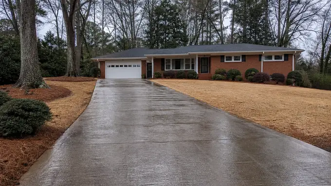 A sprayer applies sealer across a driveway. at a red-brick ranch home in Alpharetta, GA, after a rain shower.