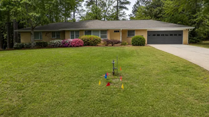 Utility flags mark buried lines before digging starts. at a buff-brick ranch home in Alpharetta, GA, under bright midday cloud.